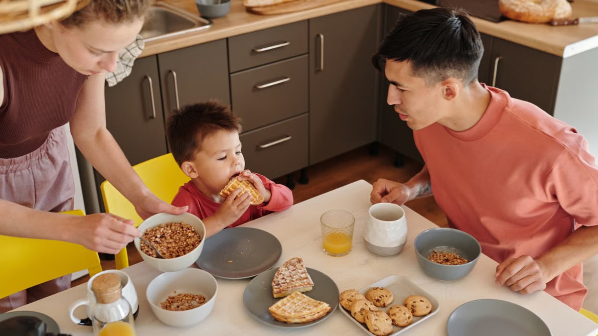 A joyful family of three sharing breakfast in a cozy kitchen setting, featuring waffles and cereal.
